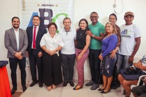 Foto mostra pessoas em pé e sorrindo em frente a um banner do Programa ABC da Cidadania.