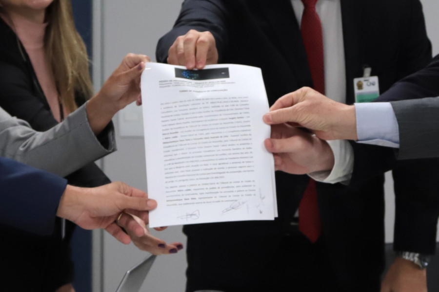 Foto mostra as mãos das pessoas participantes da audiência segurando o acordo firmado.