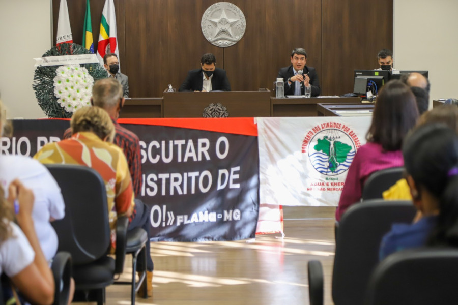 Foto mostra momento da audiência pública, com detalhe de algumas pessoas participantes sentadas e, ao fundo, a mesa principal com o conselheiro do CNJ falando e outras pessoas que a compuseram sentadas a seu lado.