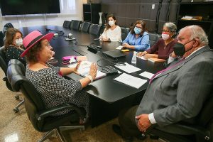 Foto mostra momento da reunião, com as pessoas sentadas em volta de uma mesa retangular.