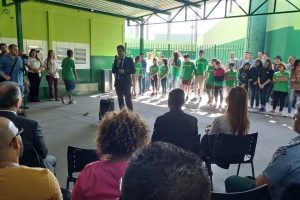 Foto de momento do evento de entrega da reforma da escola, com um homem ao centro falando e diversas outras pessoas da comunidade e alunos e alunas em volta.