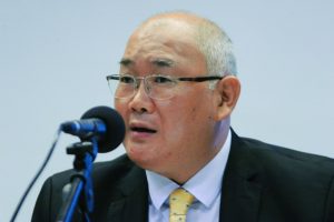 Foto mostra o conselheiro Richard Pae Kim falando em frente a um microfone de mesa.