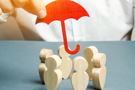 Foto mostra, em uma mesa, seis bonecos de madeira dispostos em roda. Um homem, atrás, segura sobre eles um pequeno guarda-chuva de papel.