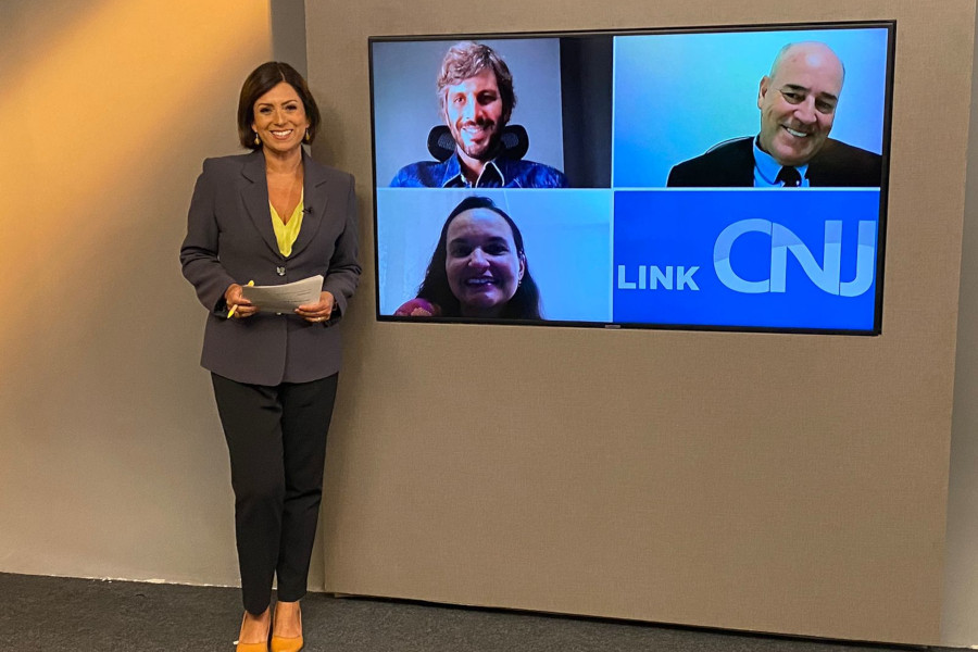 Foto do estúdio do programa mostra a apresentadora ao lado do telão onde estão as pessoas que participam como entrevistadas. Todos estão sorrindo e posando.