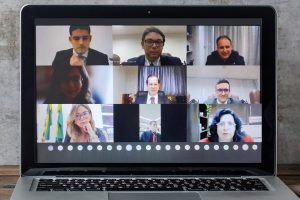 Foto de um notebook. Na tela, momento da reunião por videoconferência.