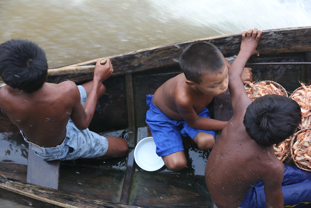 Foto mostra crianças ribeirinhas brincando em um barco na margem do rio.