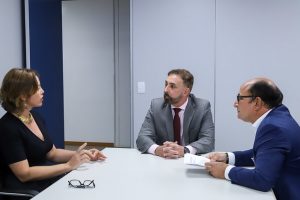 Foto mostra três pessoas sentadas em uma mesa conversando durante a reunião.