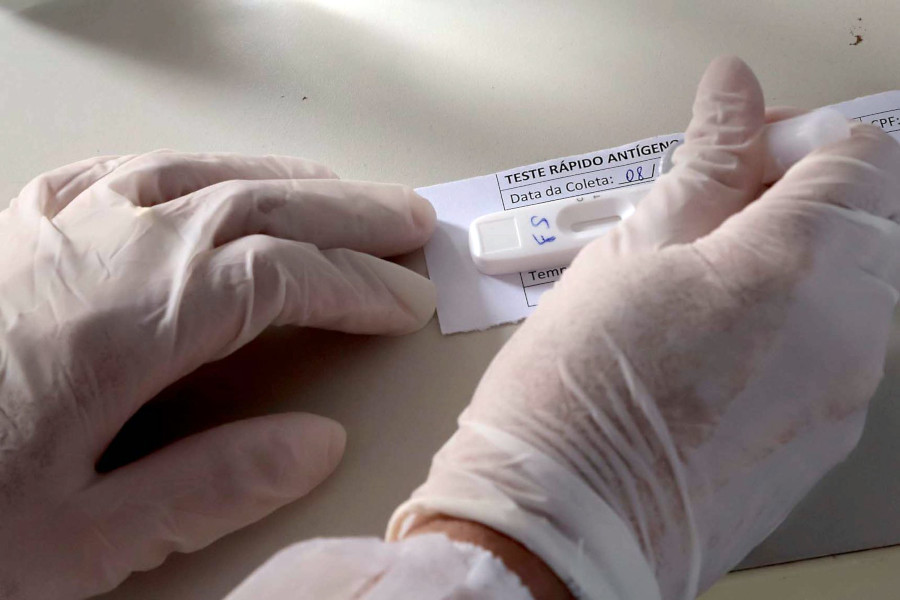 Foto mostra as mãos de uma pessoa usando luvas cirúrgicas verificando o resultado de um teste contra Covid-19.