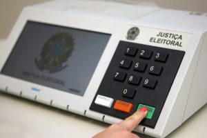 Foto de uma mulher apertando a tecla Confirma em uma urna eletrônica.