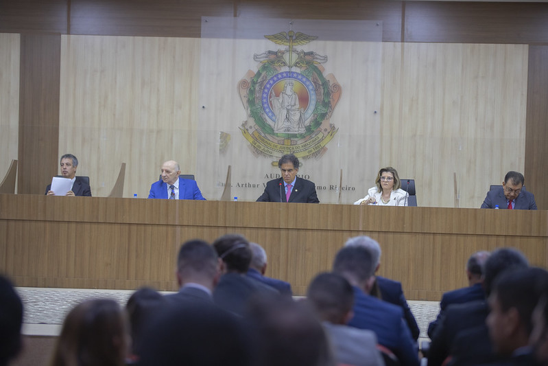 Foto do Plenário do TJAM mostra cinco pessoas sentadas na bancada durante o evento, com diversas outras assistindo na área para o público.