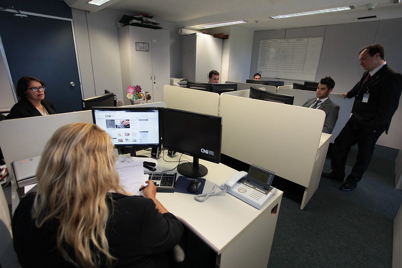 Foto mostra pessoas trabalhando em suas estações de trabalho em uma sala do CNJ.