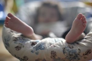 Foto mostra em destaque os pés de um bebê, com imagem fora de foco, deitada em um berço.