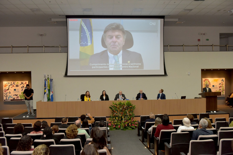 Foto mostra visão geral do auditório na Escola Judicial do TJPE. Ao fundo, em um grande telão, o ministro Luiz Fux participa por videoconferência.
