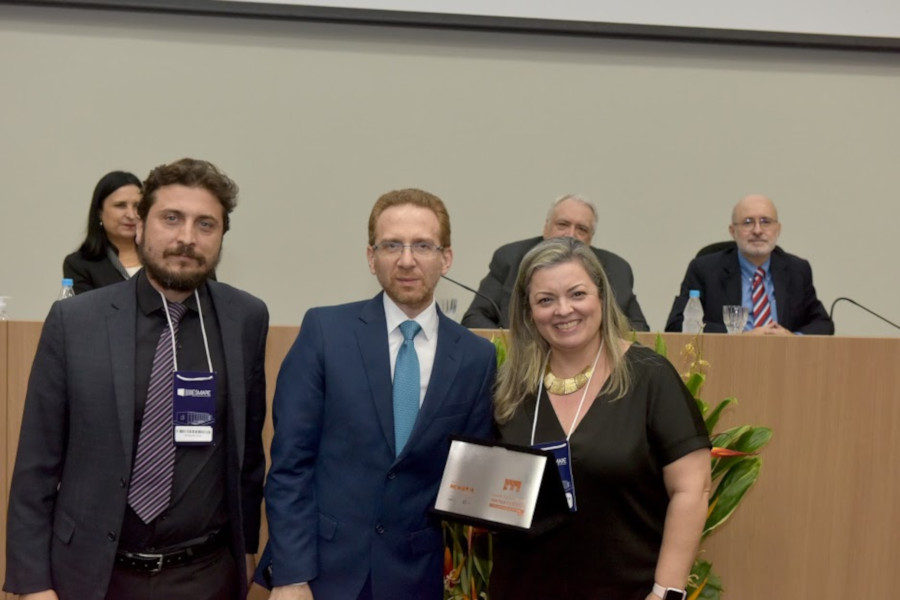 Foto mostra os três representantes do TJSP em pé, em frente ao palco do auditório, sorrindo e segurando a placa de um dos prêmios recebidos.