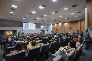 Foto mostra público e mesa de honra em um auditório de evento.