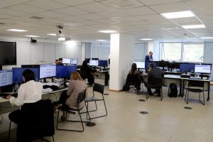 Foto mostra uma sala no CNJ com diversas pessoas sentadas em computadores e trabalhando.