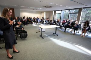 Foto mostra momento do curso, com participantes em uma grande sala sentados em forma de U.