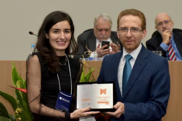 Foto mostra a pesquisadora recebendo o prêmio de um homem.