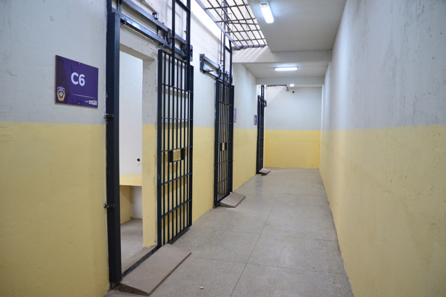 Foto mostra área interna de presídio, com três celas, estando duas fechadas com as grades e uma com as grades abertas.