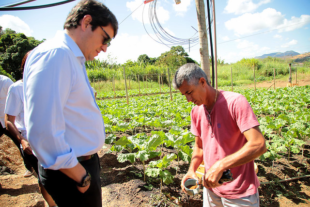 Foto mostra o conselheiro conversando com um produtor rural em frente à plantação.