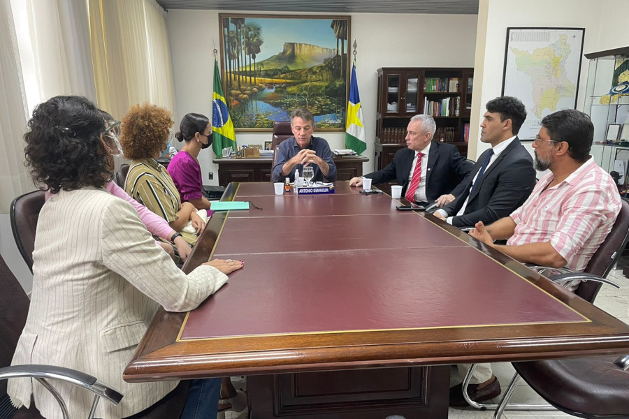 Foto mostra sete pessoas sentadas em uma mesa comprida e conversando em gabinete do TJRR.