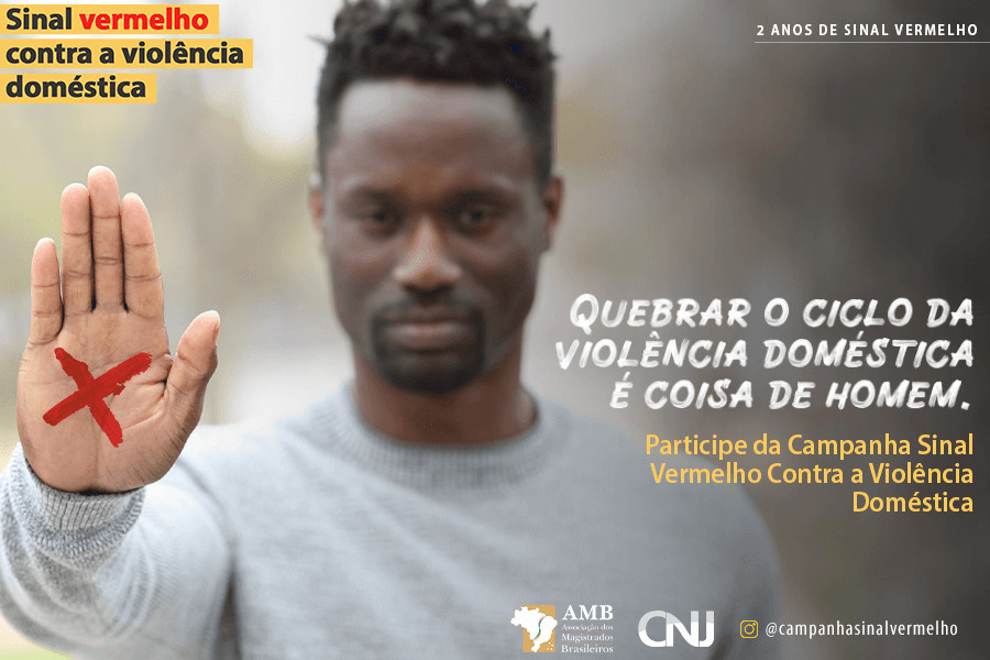 Foto mostra um homem negro com a mão levantada em sinal de Pare. Na palma da mão dele, tem um X pintado em vermelho. Texto: Sinal vermelho contra a violência doméstica. 2 anos de Sinal Vermelho. Quebrar o ciclo da violência doméstica é coisa de homem. Participe da Campanha Sinal Vermelho contra a Violência Doméstica.