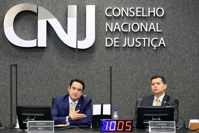 Foto mostra os conselheiros Bandeira de Mello - falando - e Marcello Terto e Silva na bancada principal do Plenário do CNJ durante a abertura do evento.
