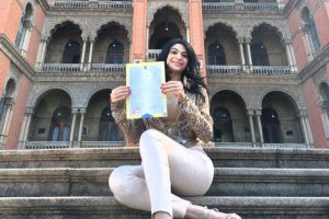 Foto mostra a mulher sentada em uma escadaria e mostrando a certidão de nascimento retificada.