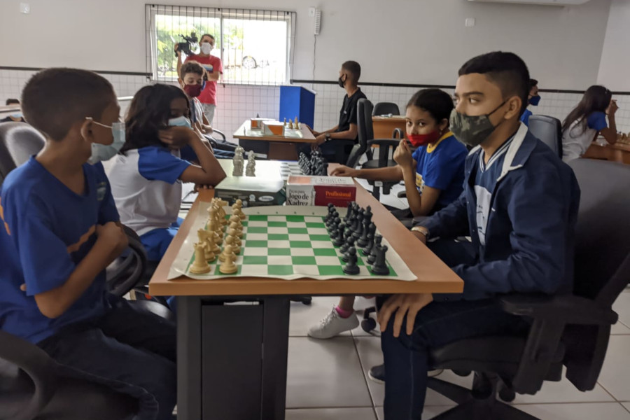 Foto mostra uma sala de escola com diversas crianças e jovens jogando xadrez.