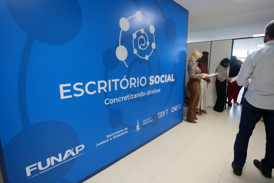 Foto de área interna do Escritório Social e uma parede tem uma grande painel com a logomarca do programa.