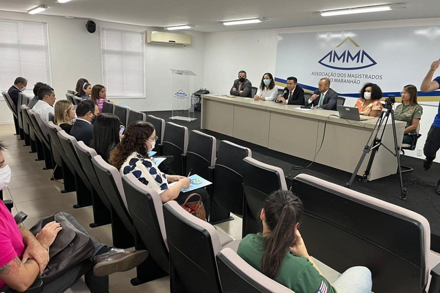 Foto mostra momento da reunião, com as pessoas sentadas em um auditório e outras seis na bancada no palco.