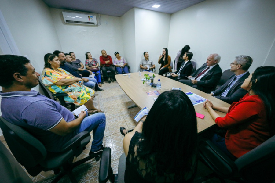 Foto mostra as 16 pessoas participantes da reunião sentadas em uma sala, em volta de uma mesa comprida.