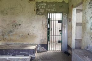 Foto mostra área interna de uma cela da UNEI Dom Bosco, com a parede toda pichada e camas e bancos de cimento depredados.