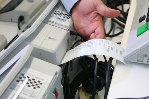 Foto de um homem segurando um boletim de urna que está sendo impresso em uma urna eletrônica.