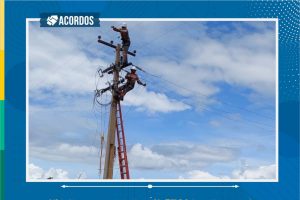 Foto de dois homens arrumando fios em um poste de energia.