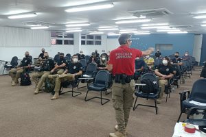Foto mostra sala de aula com o instrutor (em que se lê Polícia Judicial na camisa) e participantes da formação teórica.