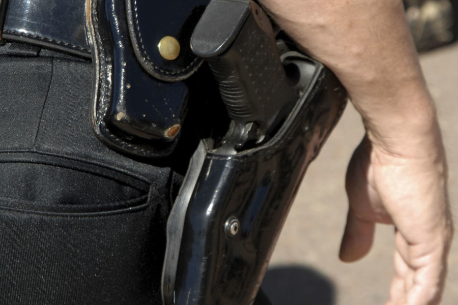Foto mostra detalhe de arma em coldre na cintura de um homem.
