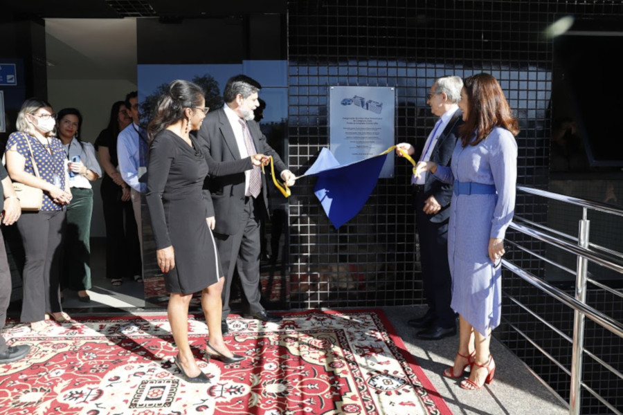 Foto mostra momento em que a placa de inauguração na parede externa da sede do TRT23 foi descerrada, com diversas pessoas assistindo.