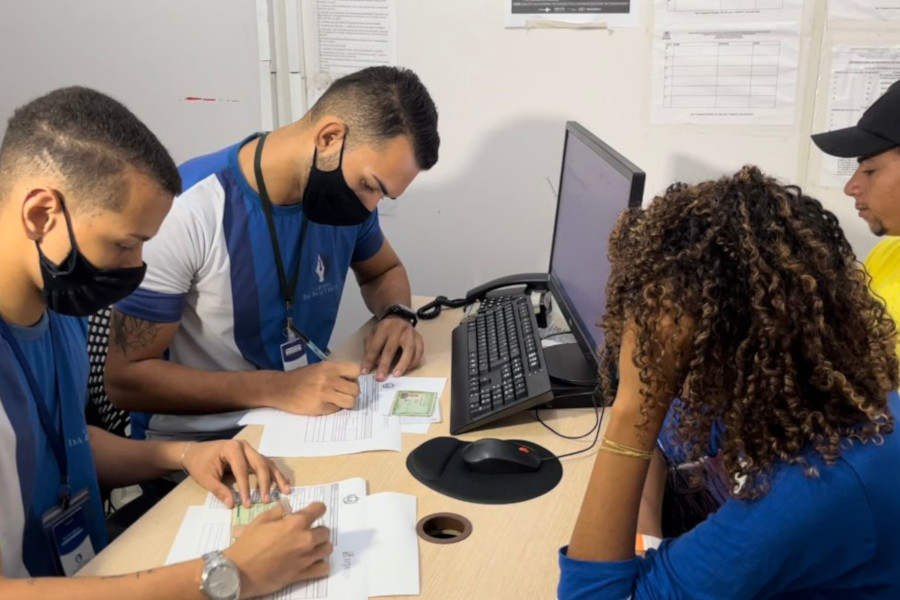 Foto mostra dois homens atendendo, com um computador à frente, um homem e uma mulher durante o Mutirão da Cidadania.
