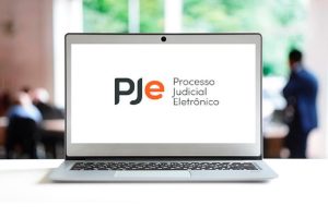 Foto mostra um notebook e, na tela, a logomarca do PJe.