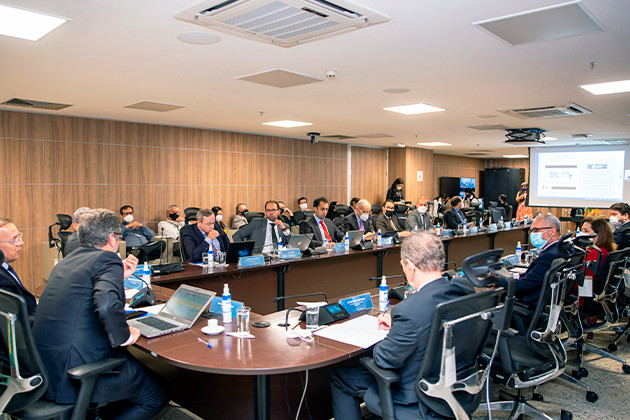 Foto mostra momento da reunião em sala do TJGO, com uma longa mesa em U e diversas pessoas sentadas em volta. Ao fundo, um telão com a apresentação que está sendo feita no momento.