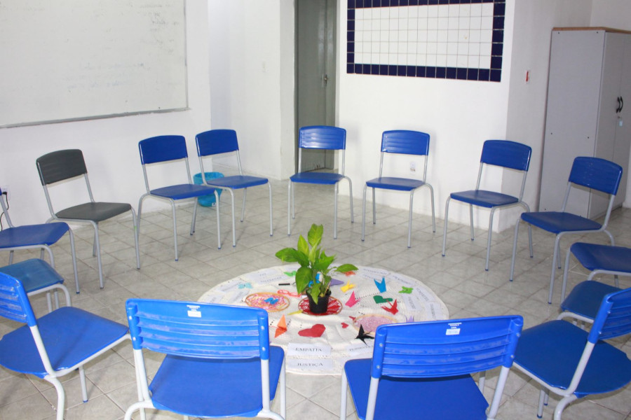 Foto mostra visão da sala na Penitenciária Feminina onde serão realizadas as atividades, com um círculo formado de cadeias e, no centro, objetos de suporte que são utilizados.