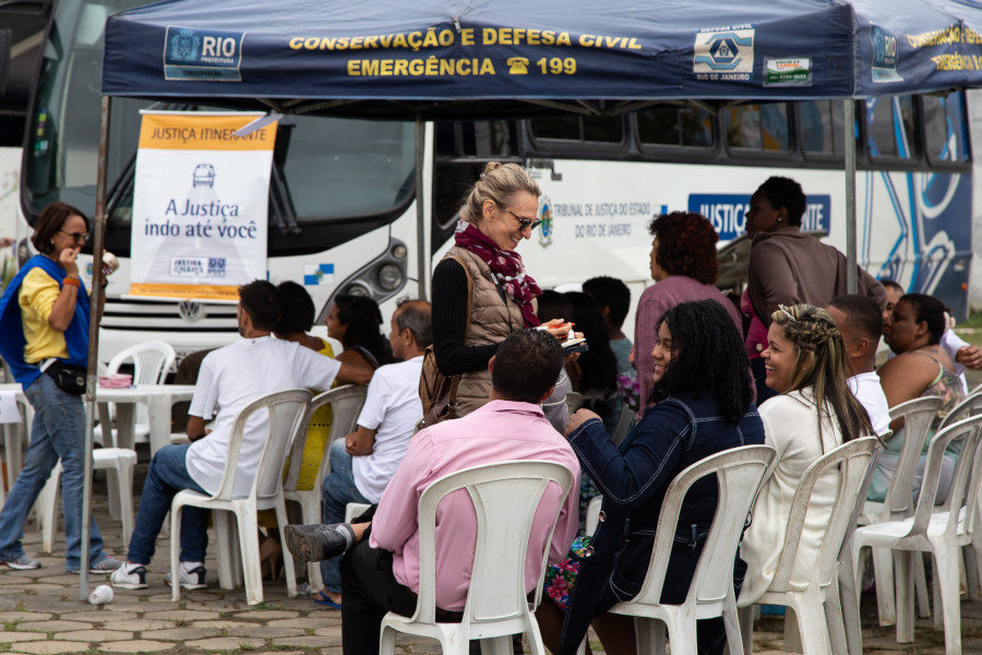 Foto mostra a desembargadora conversando com pessoas que aguardam ser atendidas que estão sentadas em frente ao ônibus do programa.