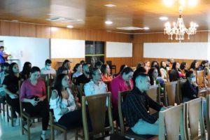 Foto mostra diversas pessoas sentadas assistindo à audiência pública em um auditório.