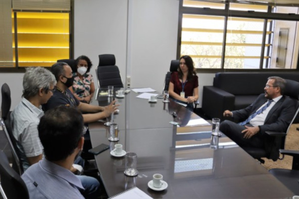 Foto mostra uma sala de reunião, com componentes da comissão conversando ao redor de uma mesa comprida.