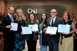 Foto no Plenário do CNJ mostra as seis pessoas da equipe do CJF em pé, sorrindo e cada uma segurando um certificado de premiação.