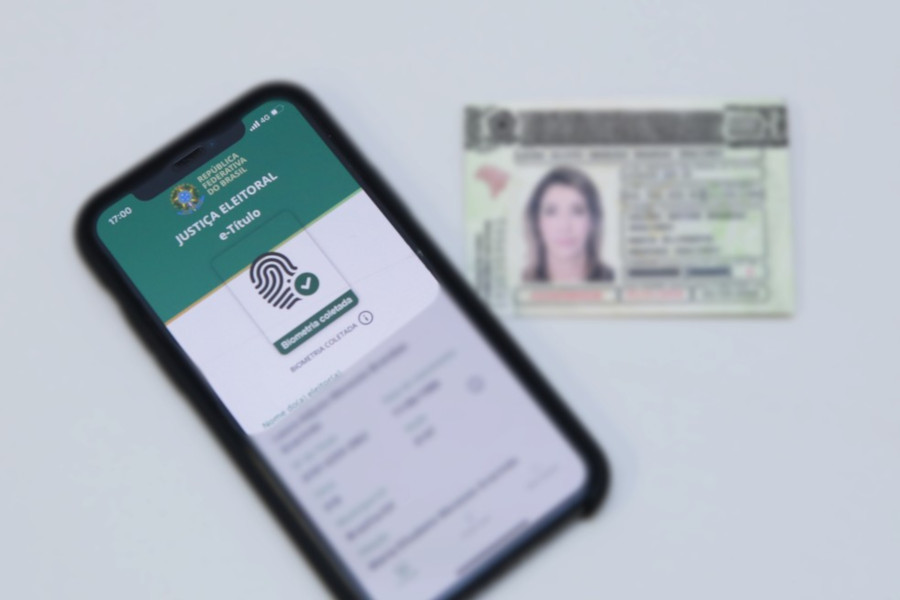 Foto mostra um título de eleitor e um celular acessando o aplicativo e-Título.