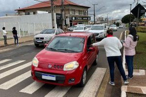 Foto mostra duas mulheres ao lado de um carro, na rua, entregando um folder da campanha.