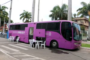 Foto do ônibus estacionado e, do lado de fora, cadeiras e mesas de plástico usadas nos atendimentos.