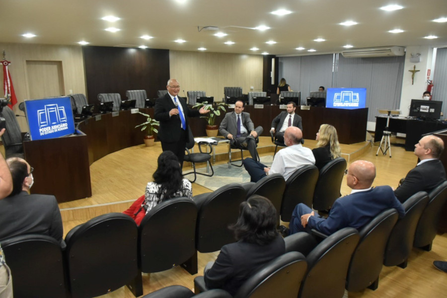 Foto no plenário do TJRR mostra o conselheiro Pae Kim em pé falando com os membros do Comitê que estão sentados em uma área de cadeiras para o público.